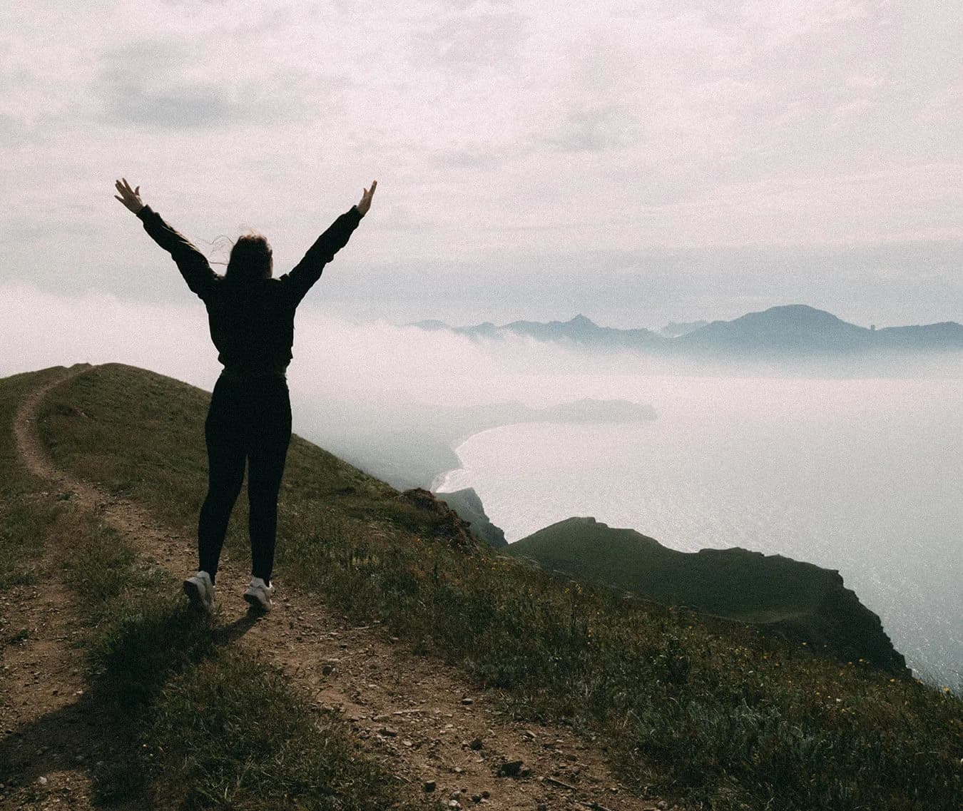 A woman with arms raised on a mountain summit above the clouds